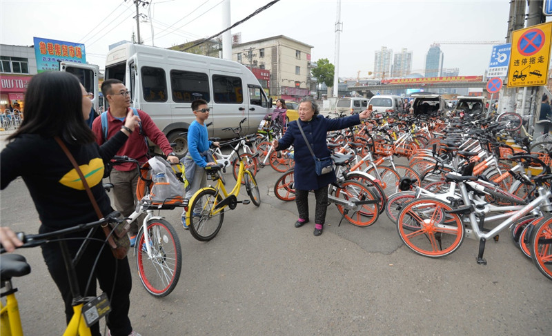 在武漢市光谷廣場附近一馬路邊，一小區門衛王大媽（中）在小區門口引導共享單車騎行者文明停放（4月3日攝）。